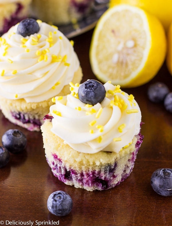 These Lemon Blueberry Cupcakes are bursting with vanilla, fresh blueberries and aย hint of lemon. Piled high with a delicious lemon buttercream frosting and of course, it wouldnโt be a cupcake with out SPRINKLES! Two lemon Blueberry Cupcakes.
