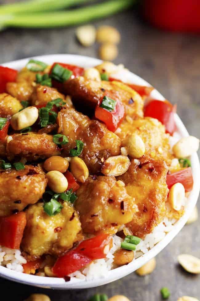 Delicious breaded chicken coatedย in a sweet and spicy sauce with peppers and peanuts hidden throughout. This is WAY better than any takeout you will have! Baked Kung Pao chicken over white rice in a bowl.