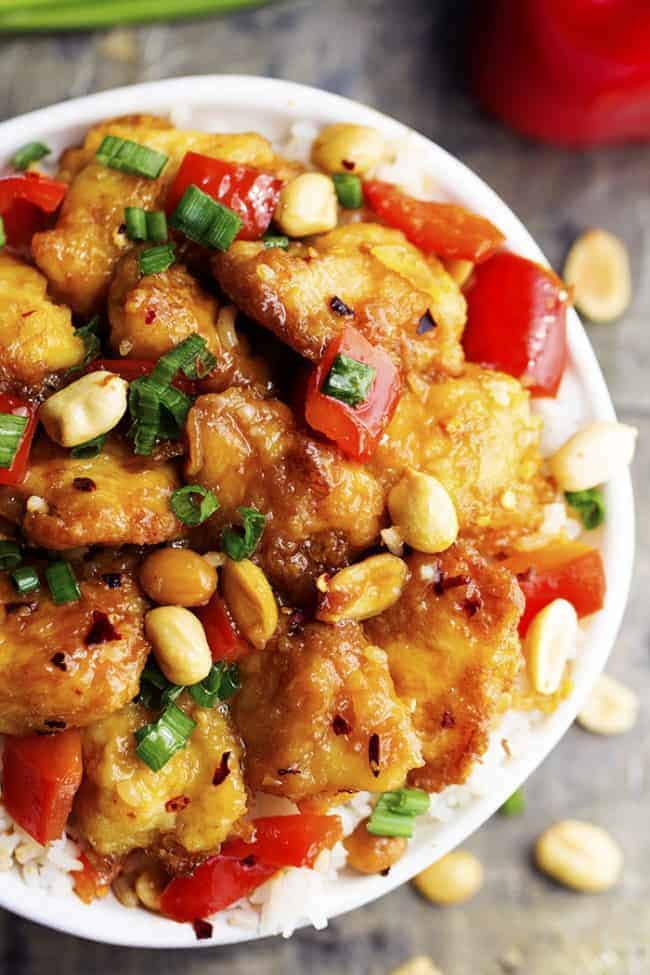 Delicious breaded chicken coatedย in a sweet and spicy sauce with peppers and peanuts hidden throughout. This is WAY better than any takeout you will have! Baked Kung Pao chicken in a bowl with white rice and garnished with peanuts.