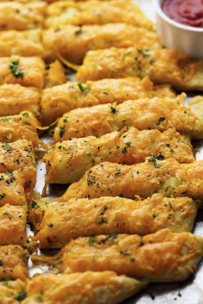 Delicious and cheesy cheddar garlic breadsticks that are made with a quick and easy dough recipe! These will be in and out of the oven in no time and you won't be able to stop eating them! cheesy garlic sticks on a tray.