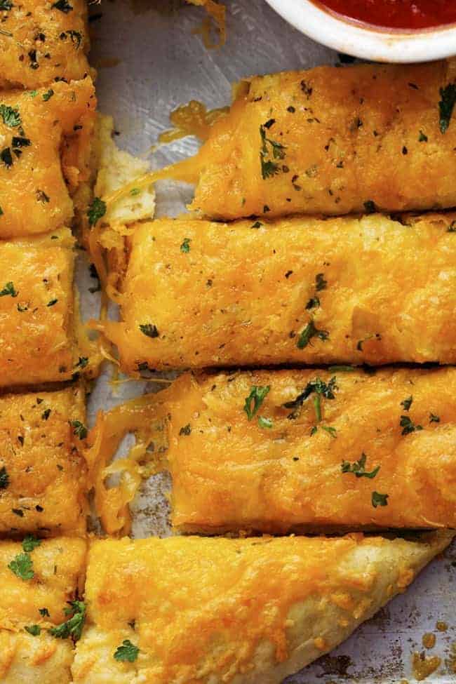 Delicious and cheesy cheddar garlic breadsticks that are made with a quick and easy dough recipe! These will be in and out of the oven in no time and you won't be able to stop eating them! Areal view of cheesy garlic sticks.