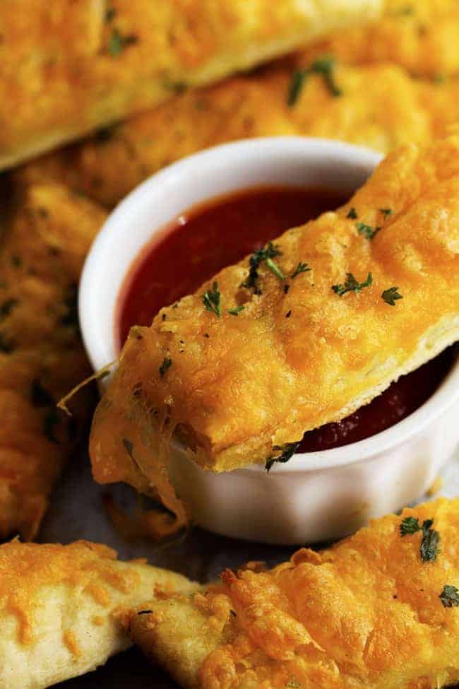 Delicious and cheesy cheddar garlic breadsticks that are made with a quick and easy dough recipe! These will be in and out of the oven in no time and you won't be able to stop eating them! cheesy garlic stick dipping in sauce.