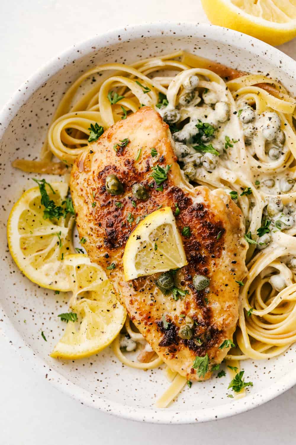 This creamy lemon chicken piccata is a quick and easy one-pot meal that's on the dinner table in 30 minutes! Tender breaded chicken in a creamy lemon sauce that the entire family will love. Chicken breasts with lemon piccata sauce on a bed of noodles in a white bowl.