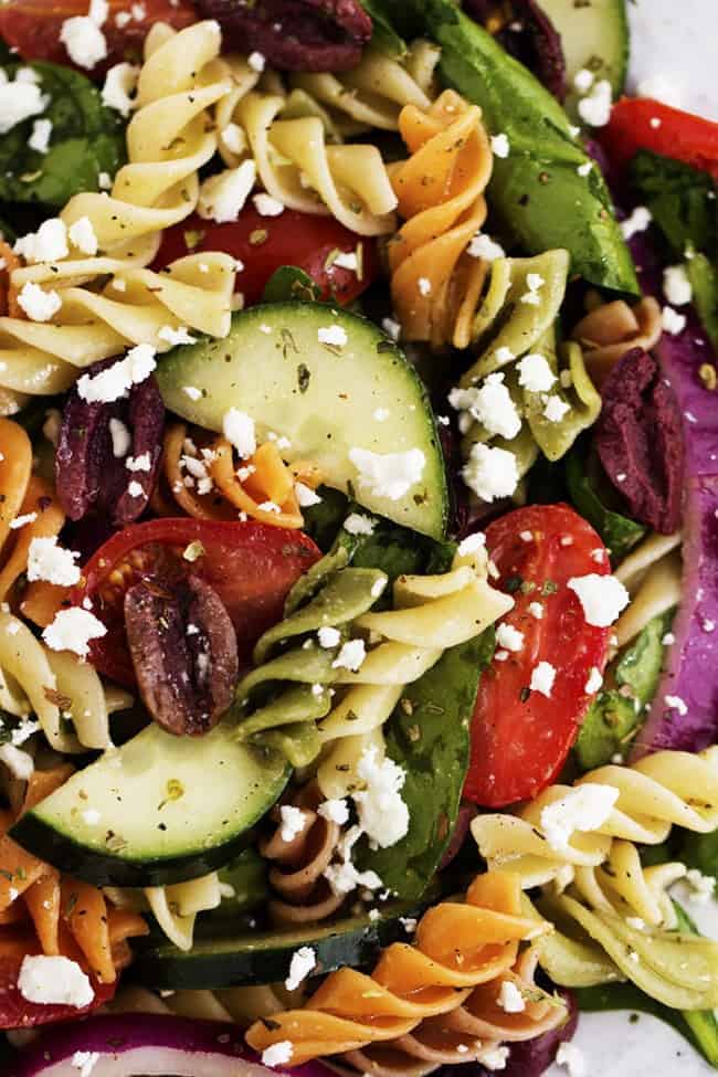 Fresh Spinach combined with olives, red onion, tomatoes, cucumber, and sprinkled with feta cheese. The pasta adds a delicious texture and is tossed with a red wine vinaigrette. greek pasta salad close up.