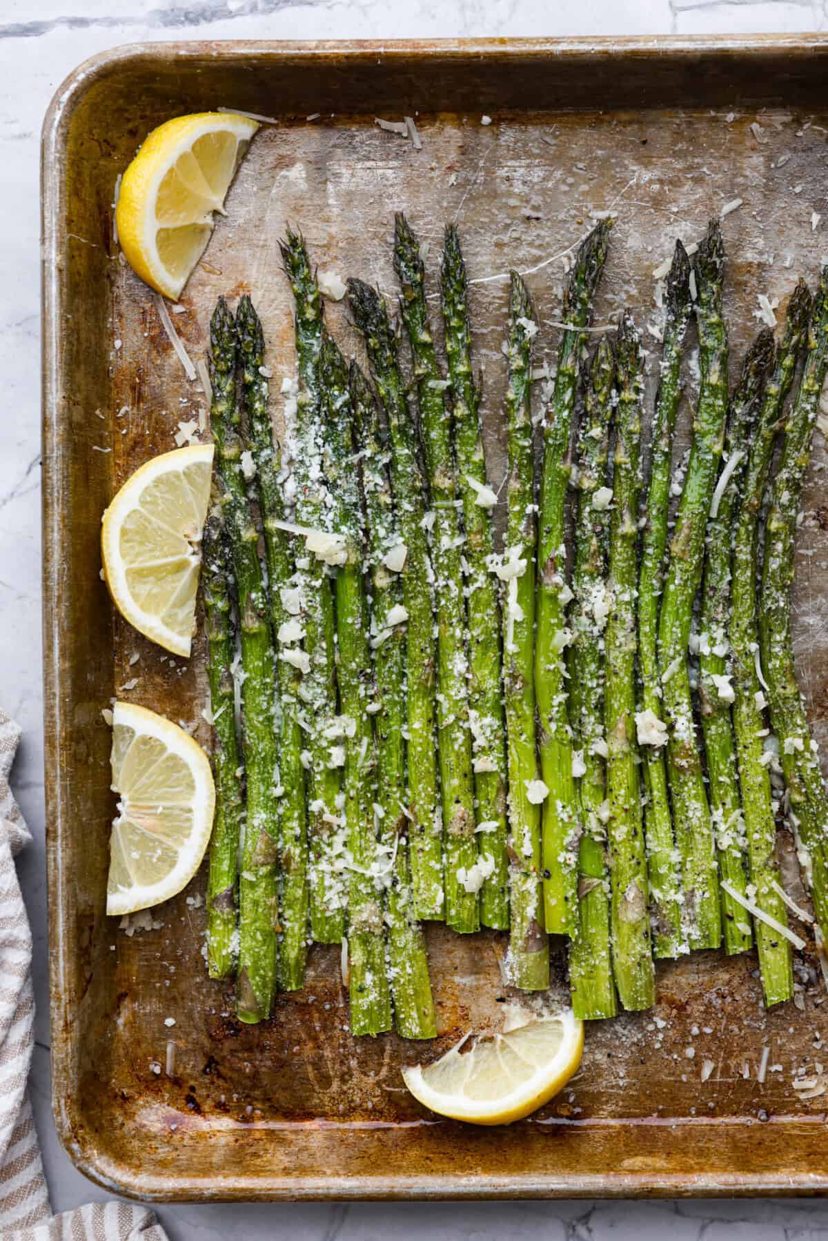 You'll love the combination of flavors in this roasted lemon parmesan garlic asparagus! It's a quick and easy side dish bursting with parmesan, garlic, and a hint of lemon to brighten it all. This is a side that you will make again and again! Top view of roasted lemon parmesan garlic asparagus on a sheet pan with lemons.