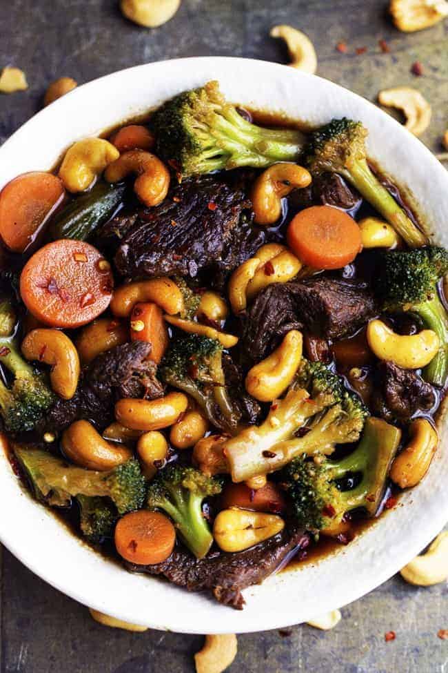 Delicious melt in your mouth beef that cooks right in your slow cooker with veggies and cashews hidden throughout. One of the best meals that you will make in your slow cooker and so much better than takeout! slow cooker cashew beef and broccoli in a white serving dish.