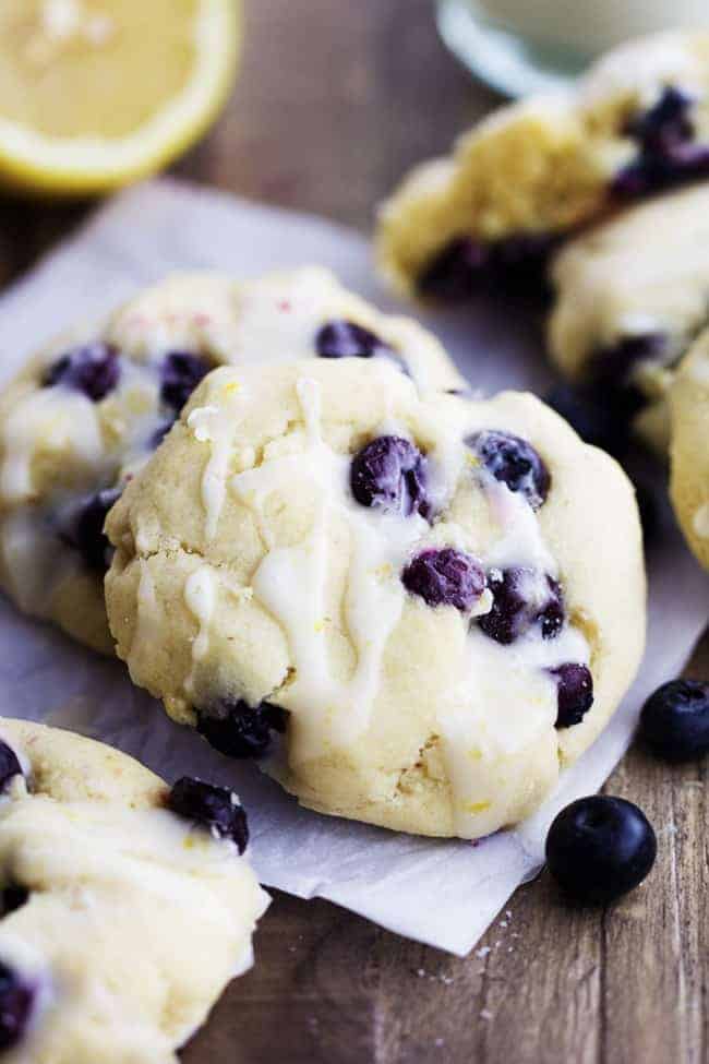 Perfect moist and puffy cookies with fresh blueberries bursting inside. These cookies are a mix between a blueberry muffin and a soft and chewy cookie. Drizzled in a lemon glaze, these will become a new favorite! Close up on two blueberry cream cheese cookies.