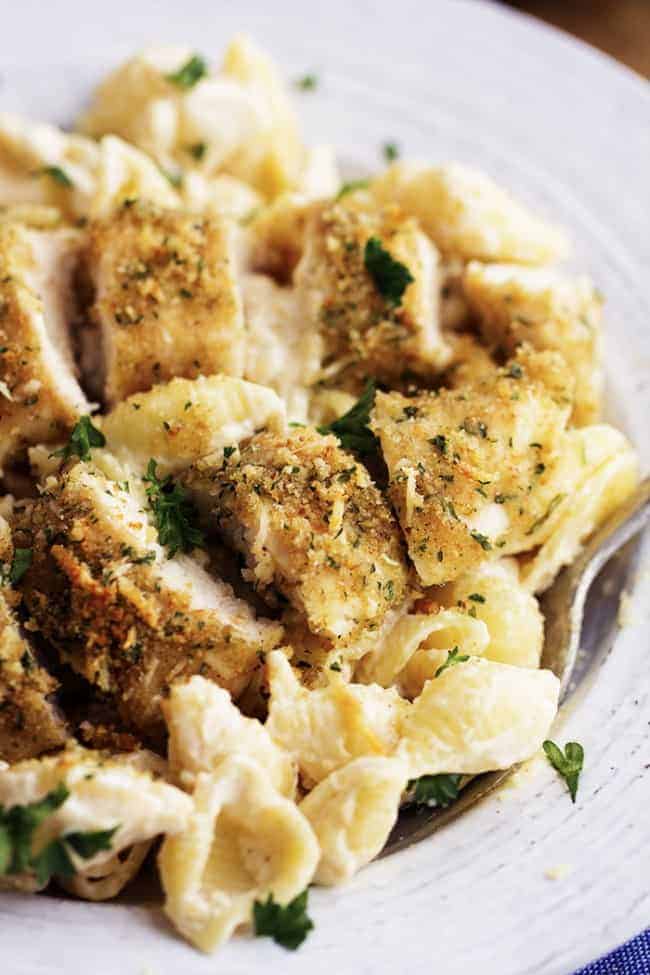 The most creamy and delicious homemade garlic alfredo shells topped with crispy parmesan garlic chicken. This is an absolutely fantastic meal that will instantly become a family favorite! Scooping a spoonful of creamy garlic noodles and chicken out of a white bowl.