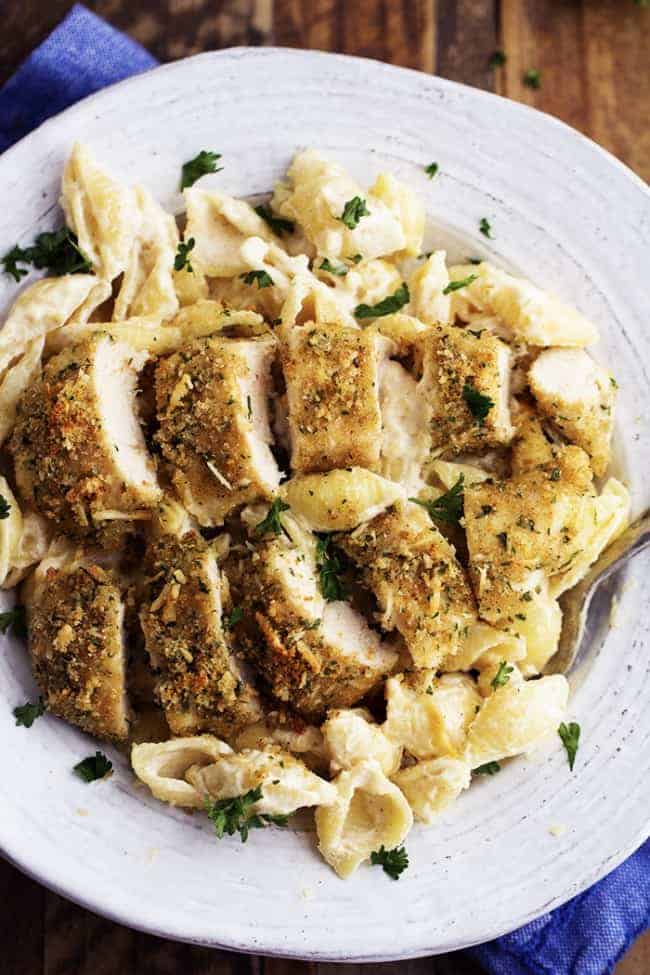 The most creamy and delicious homemade garlic alfredo shells topped with crispy parmesan garlic chicken. This is an absolutely fantastic meal that will instantly become a family favorite! creamy garlic alfredo on a white plate.