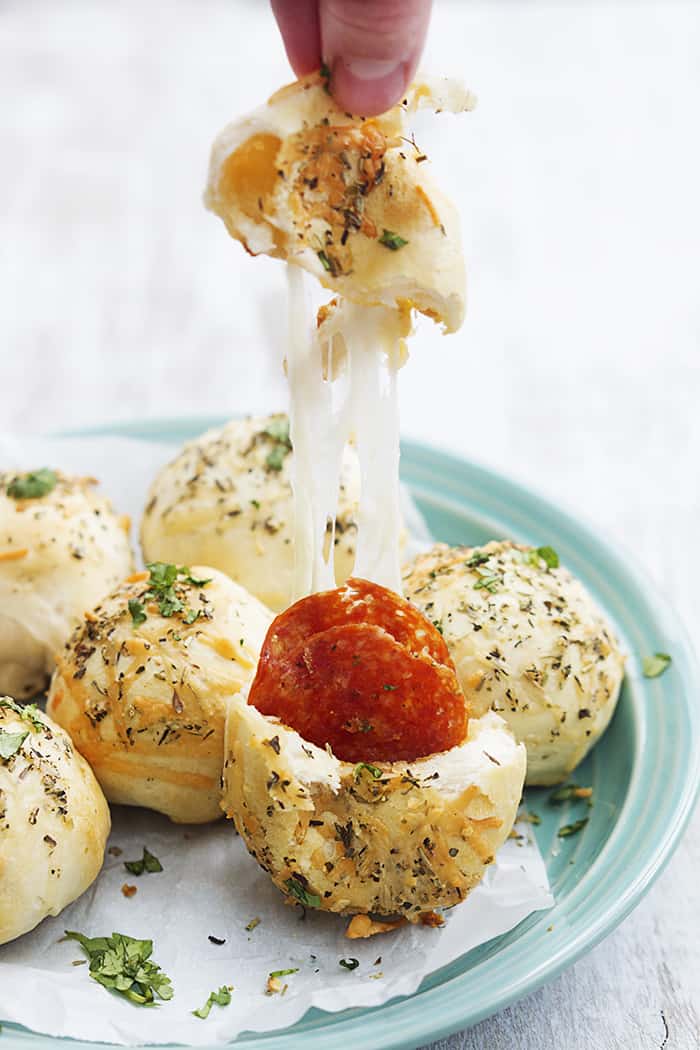 These cheesy pepperoni bombs are perfect for a snack or appetizer… or if you’re like me, for dinner! Pulling apart a pepperoni bomb to show gooey cheese and a pepperoni inside.