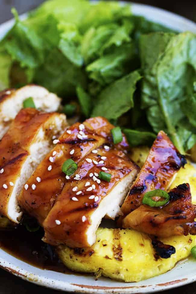 The most delicious sweet pineapple teriyaki glaze coats this chicken perfectly. It grills to juicy and tender perfection on the BBQ and will be one of the best things you grill this summer! pineapple teriyaki chicken with pineapple and salad on a white plate.