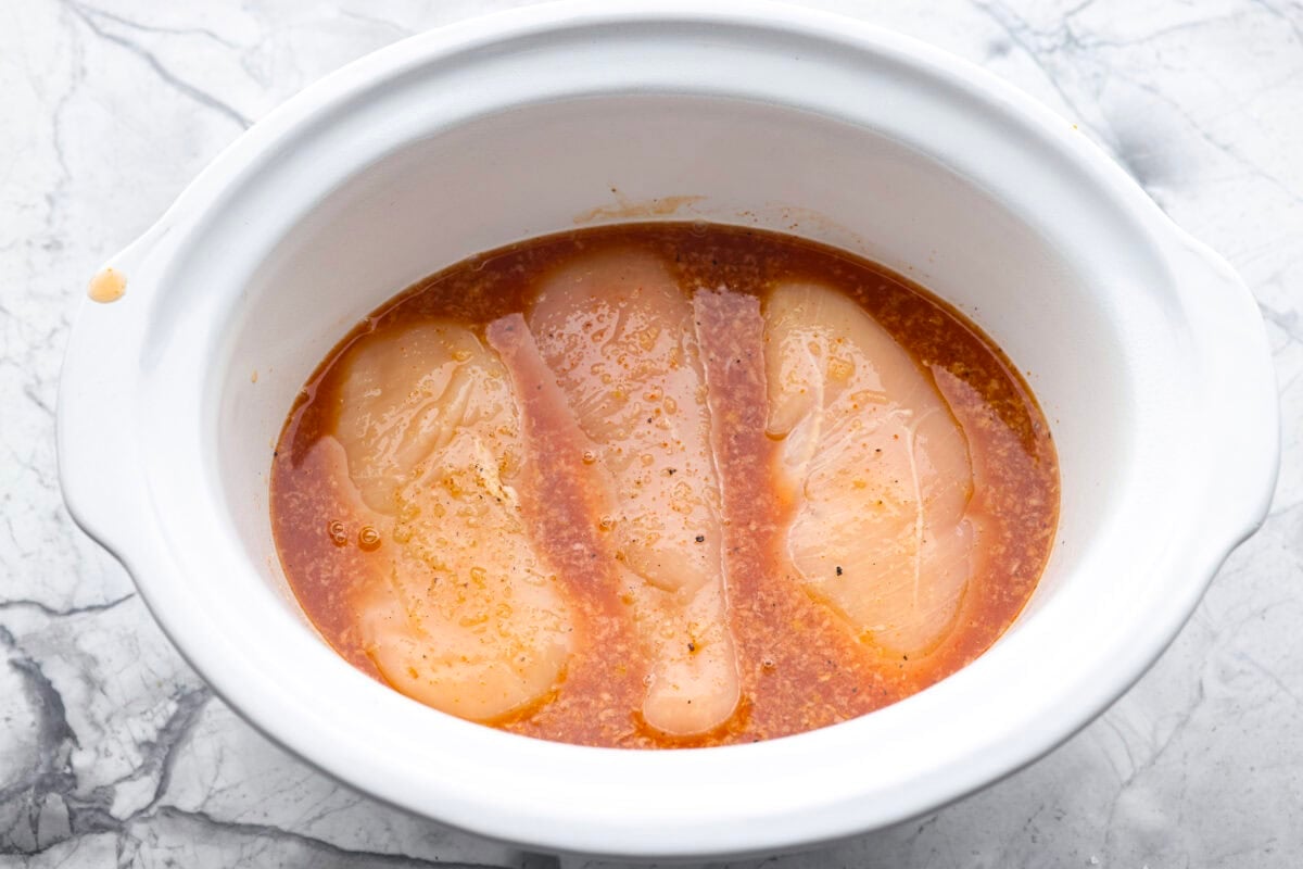 My spicy Slow Cooker Honey Sriracha Chicken is moist, tender, and out-of-this-world delicious with the sweet and spicy sauce! If you love sriracha, you'll love this! Whisked sauce poured over the chicken in the crock pot.