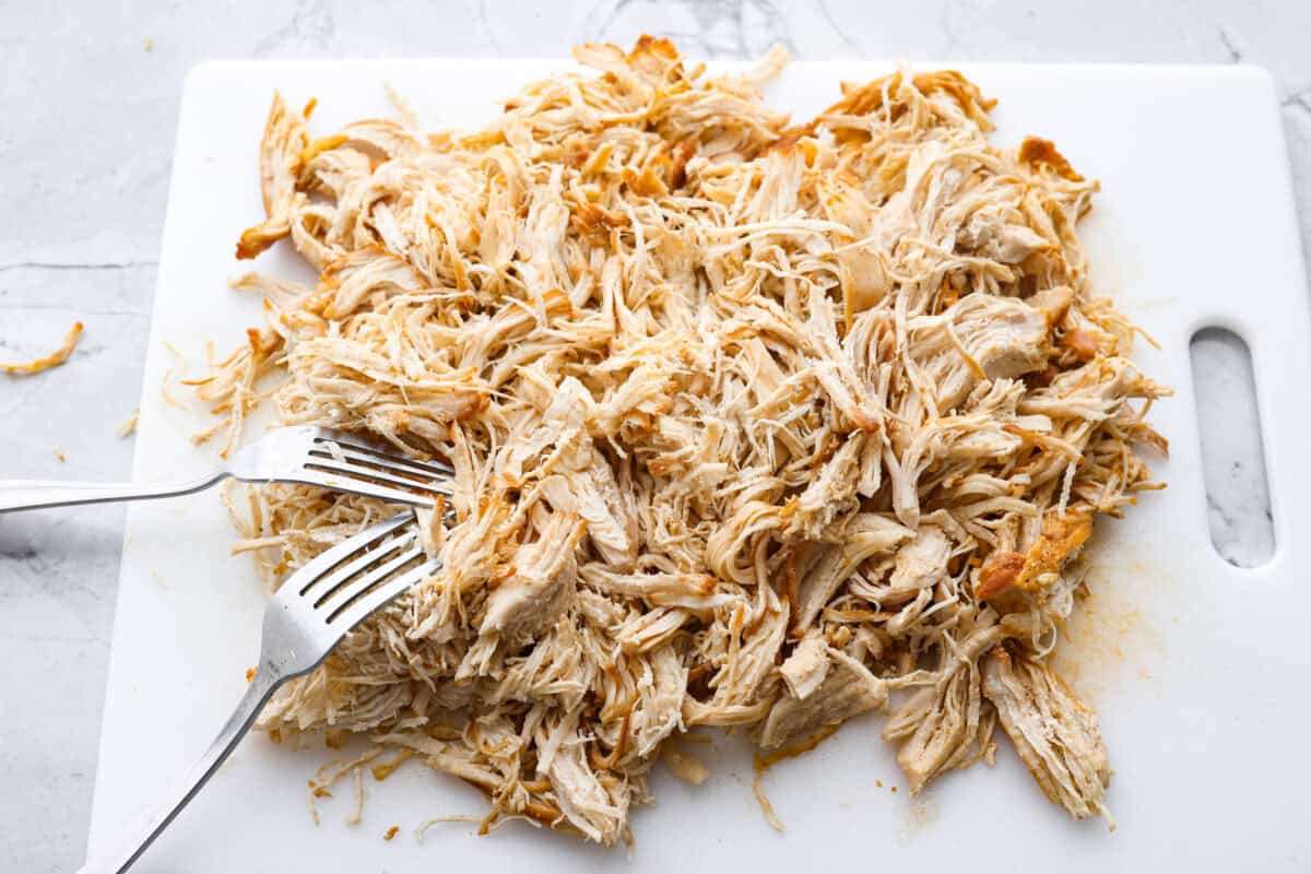 My spicy Slow Cooker Honey Sriracha Chicken is moist, tender, and out-of-this-world delicious with the sweet and spicy sauce! If you love sriracha, you'll love this! Cooked chicken on a cutting board being shredded with forks.