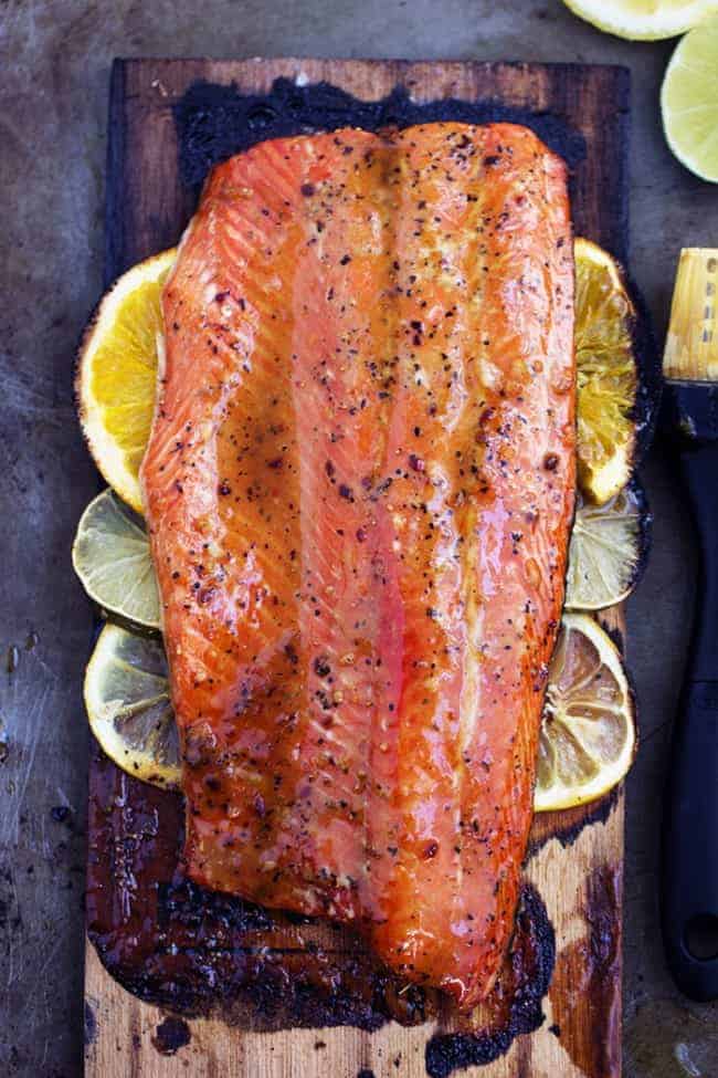 A five starย salmon recipe that gets infused with a lemon, lime and orange marinade. It grills to tender and flaky perfection and has the best sweet and tangy flavor! grilled triple citrus salmon on lemon slices on a wooden plank.