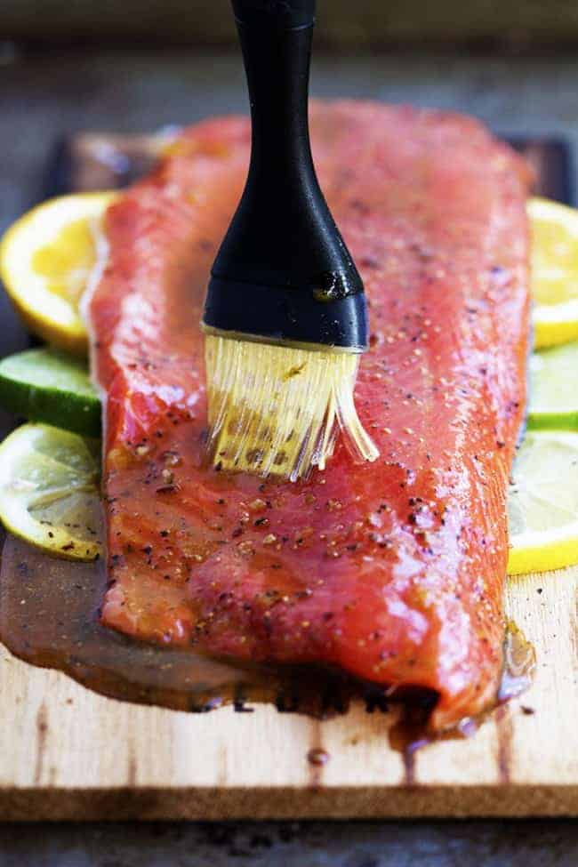 A five starย salmon recipe that gets infused with a lemon, lime and orange marinade. It grills to tender and flaky perfection and has the best sweet and tangy flavor! Brushing grilled salmon with sauce.