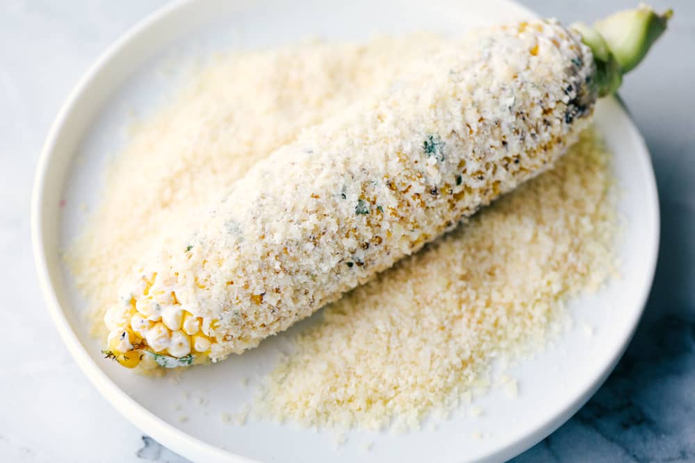 This corn gets grilled and slathered with an amazing mayonnaise blend and topped with parmesan cheese and chili powder. This is one of the best corn recipes you will eat! Grilled corn coated with mayonnaise and being rolled in Parmesan cheese.