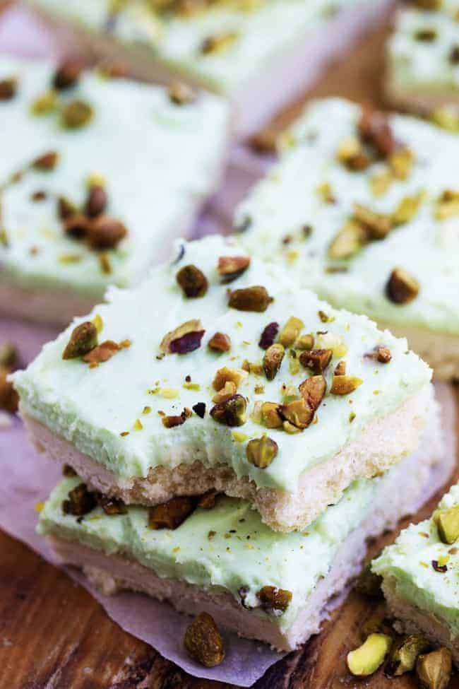 A creamy and a delicious pistachio dessert on top of a buttery shortbread crust. This dessert is quick and easy and perfect for your next potluck! pistachio bars in a stack with a bite taken out of the top bar.