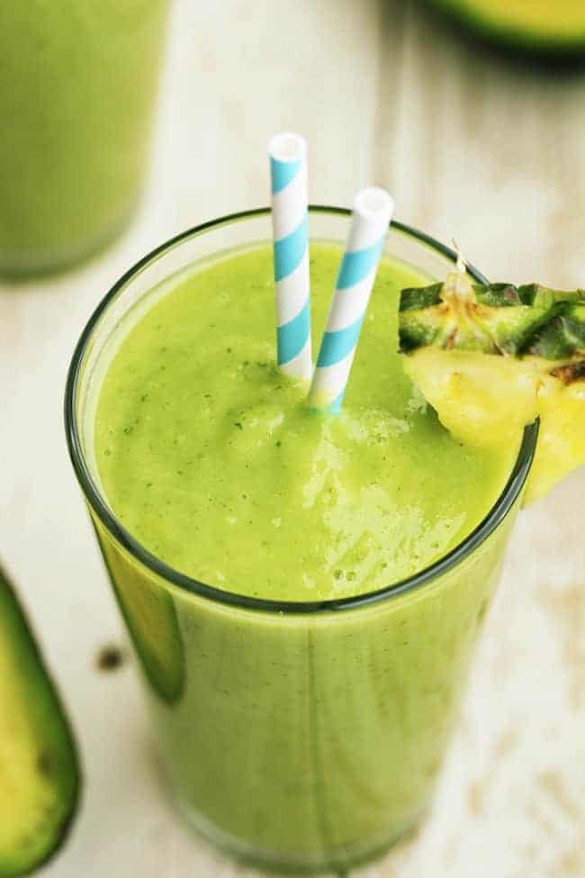 This delicious and perfectly smooth avocolada smoothie combines avocado, pineapple, spinach, kale, coconut, and lime. It's SOO GOOD that you will want one every day! Avocolada smoothie in a glass with two striped straws.