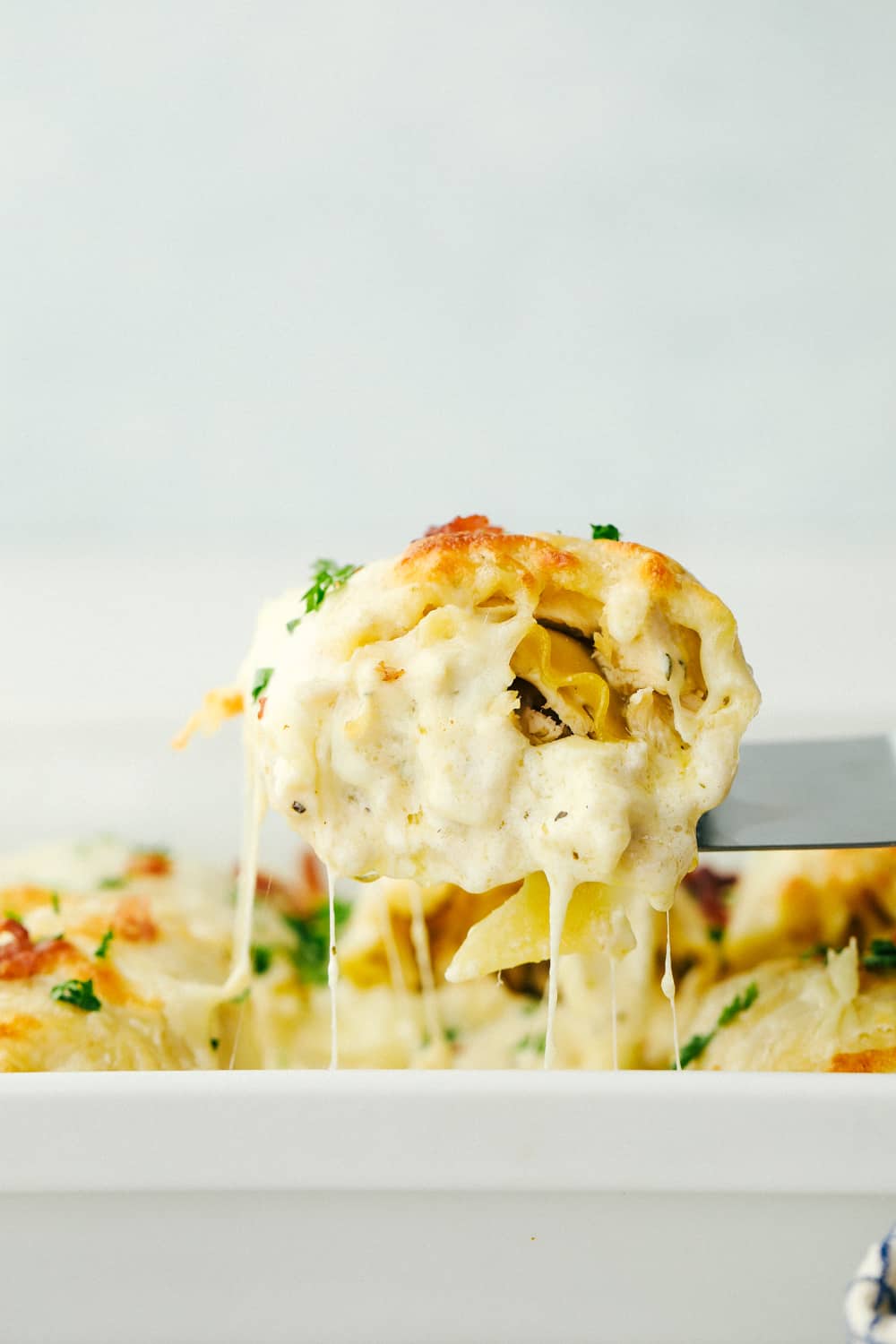 Alfredo Roll Ups are cheesy, perfectly portioned servings of deliciousness. This is going to be one of the best meals you will ever make! Scooping out a lasagna roll up out of the pan.