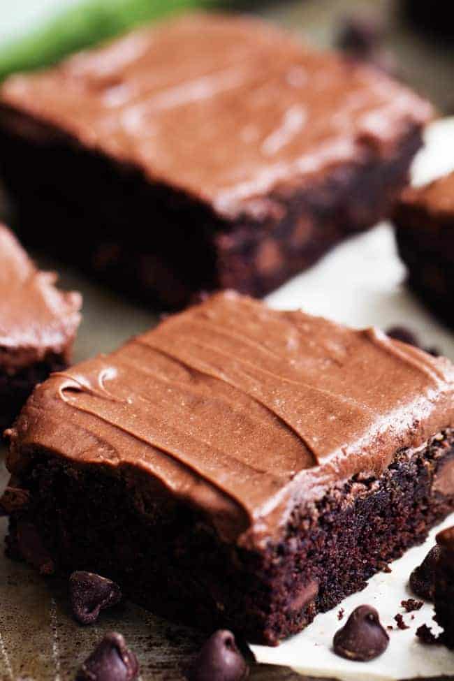 Perfectly moist and chocolatey brownies filled with chocolate chips and topped withย chocolateย frosting. Simple and delicious and you won't even be able to tell that 2 cups of zucchini is hidden inside!ย double chocolate zucchini brownies on white paper.