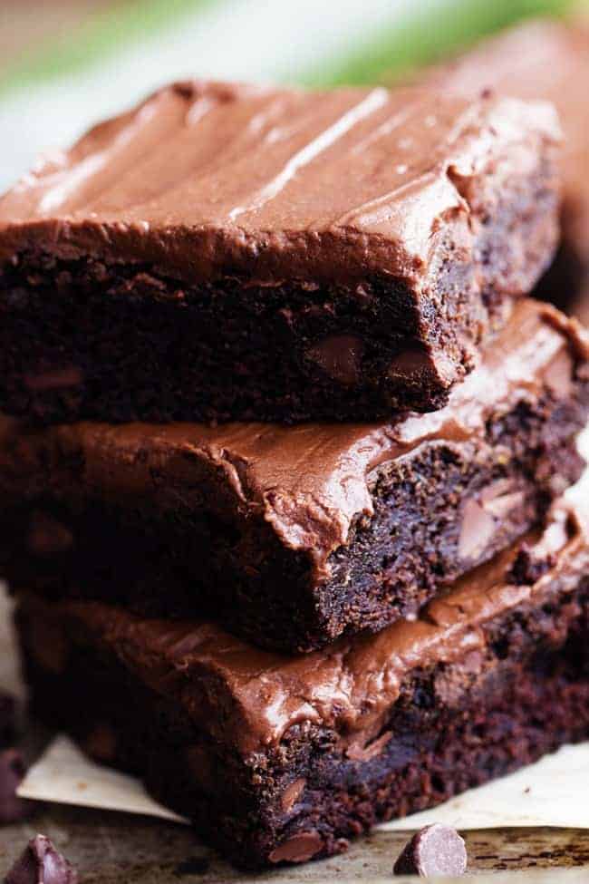Perfectly moist and chocolatey brownies filled with chocolate chips and topped withย chocolateย frosting. Simple and delicious and you won't even be able to tell that 2 cups of zucchini is hidden inside!ย zucchini brownies in a stack.