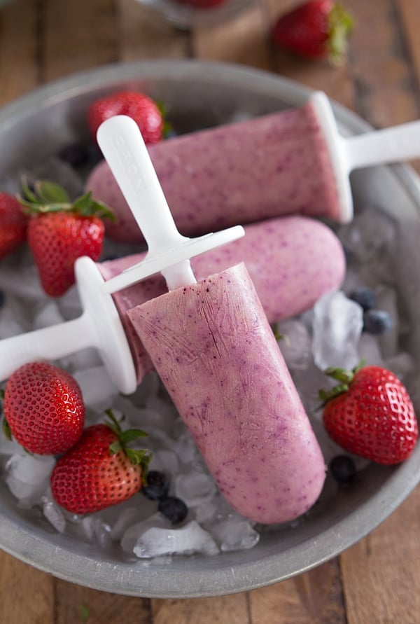 These pops are made SUPER easy. Just blend up the ingredients, put them in a popsicle maker, and freeze. Fruity Greek Yogurt Frozen Pops on top of a bowl of ice and fruit.