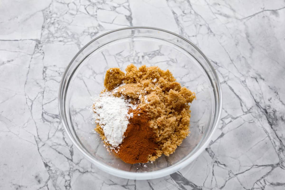 Old-fashioned peach cobbler is a timeless summer dessert! Its warm, cakey layers baked with freshly sliced peaches are a match made in heaven. Top the cobbler with vanilla ice cream, and every bite will be a delight! Overhead shot of brown sugar, cinnamon, nutmeg and cornstarch in glass bowl.