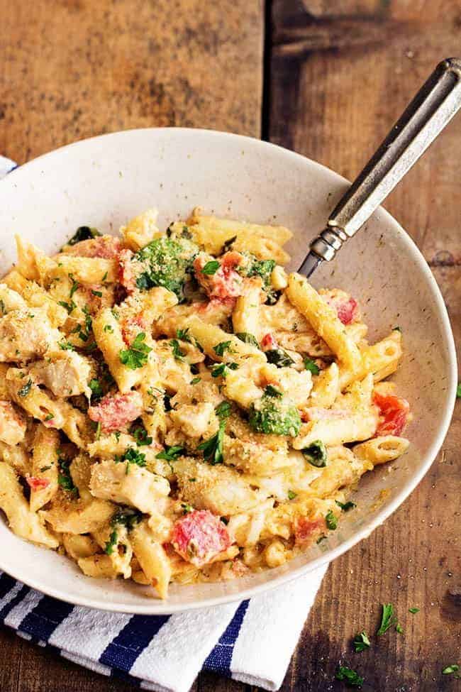 My favorite homemade garlic alfredo sauce is combined with pesto giving this casserole amazing flavor! It is creamy and delicious and sure to be a hit at the dinner table! pesto alfredo chicken casserole in a white bowl.