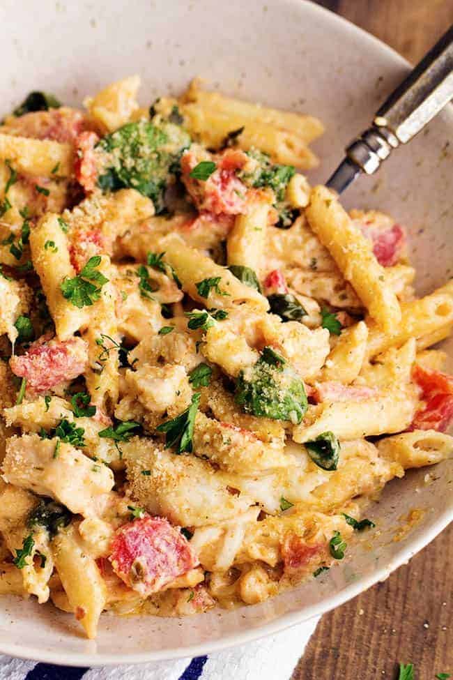 My favorite homemade garlic alfredo sauce is combined with pesto giving this casserole amazing flavor! It is creamy and delicious and sure to be a hit at the dinner table! pesto alfredo chicken casserole in a white serving bowl.