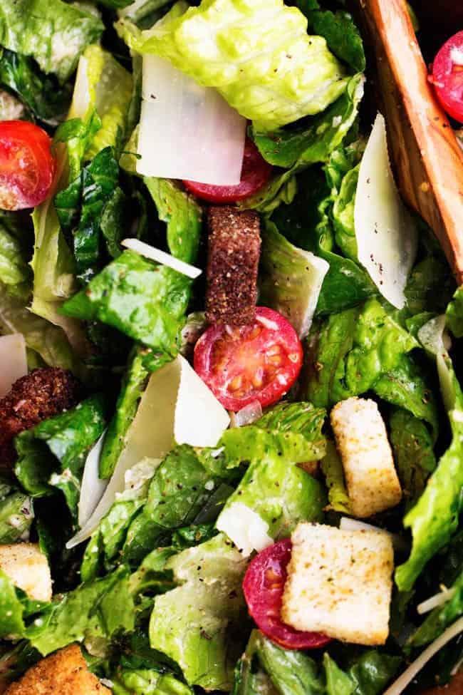 Fresh romaine and cherry tomatoes get tossed with a delicious asiago caesar dressing. Topped with shaved parmesan cheese and croutons, this is a delicious and classic salad that makes the perfect side! chicken caesar salad close up areal view.