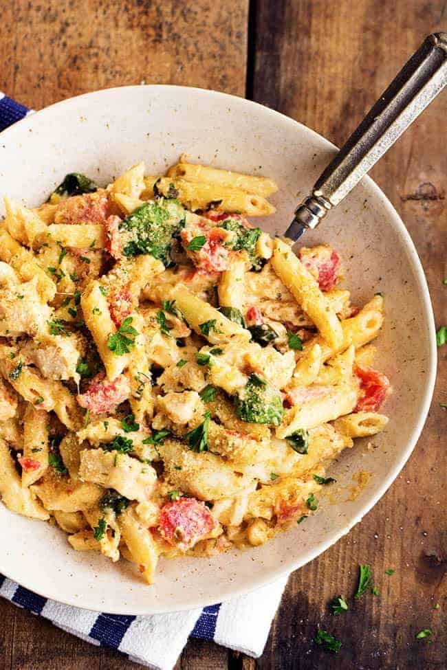 My favorite homemade garlic alfredo sauce is combined with pesto giving this casserole amazing flavor! It is creamy and delicious and sure to be a hit at the dinner table! pesto chicken alfredo casserole in a white serving dish.