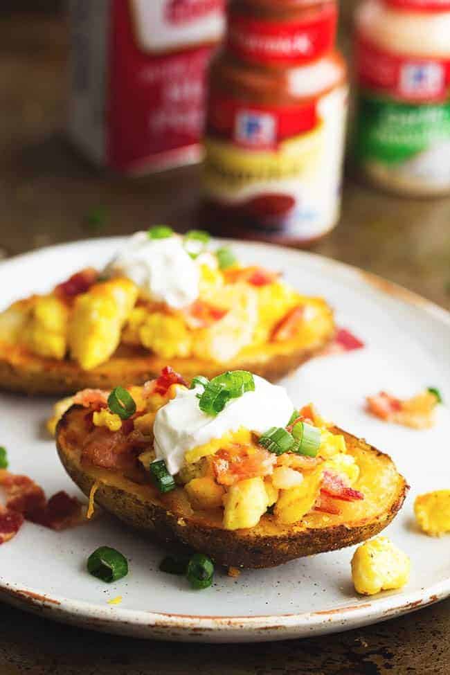 Seasoned crispy potato skins get loaded with potatoes, eggs, bacon and cheese. Topped with all of your favorite toppings, these will become a family favorite! potato skins on a white plate.