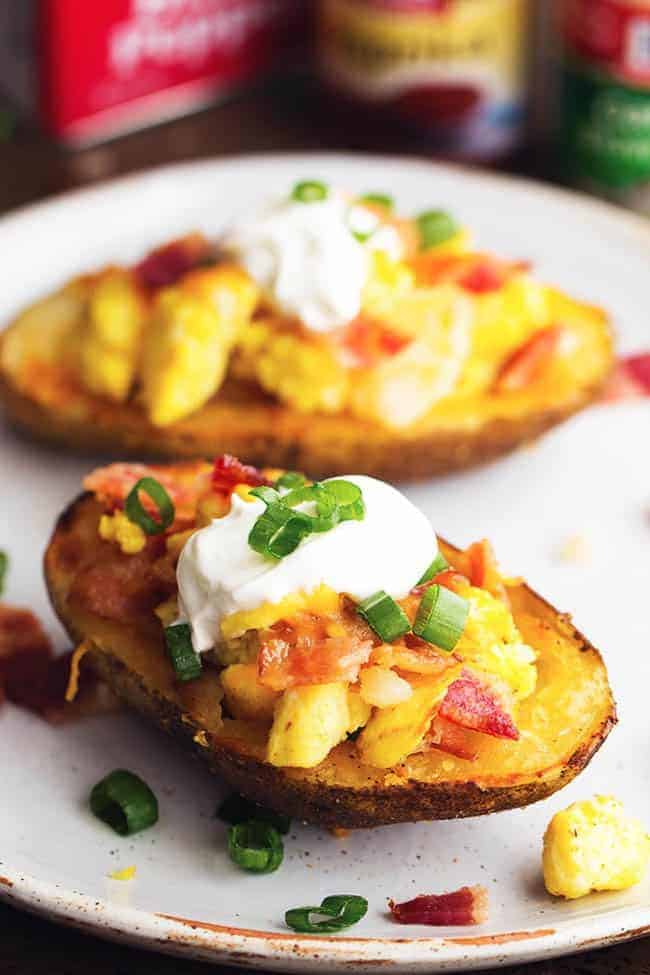Seasoned crispy potato skins get loaded with potatoes, eggs, bacon and cheese. Topped with all of your favorite toppings, these will become a family favorite! potato skins on a white plate.