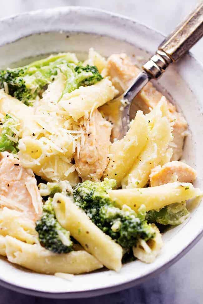 Delicious homemade three cheese alfredo gets tossed with pasta, broccoli and chicken. It is quick and easy and out of this world good! It will become an instant favorite! Three cheese chicken broccoli alfredo in a white bowl.