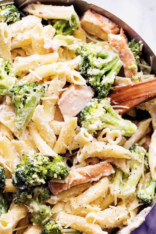 Delicious homemade three cheese alfredo gets tossed with pasta, broccoli and chicken. It is quick and easy and out of this world good! It will become an instant favorite! three cheese chicken broccoli alfredo in a pot with a wooden spoon.