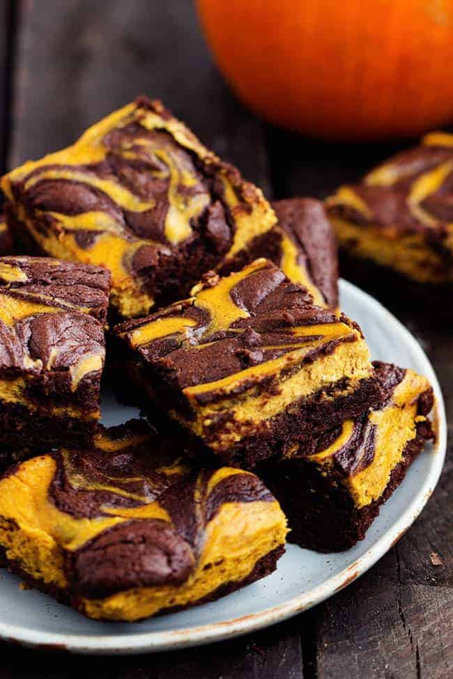 Perfectly moist and fudgy brownies swirled with pumpkin cheesecake. These are so rich and delicious and they make an amazing fall treat! pumpkin cheesecake brownies stacked on a white plate.