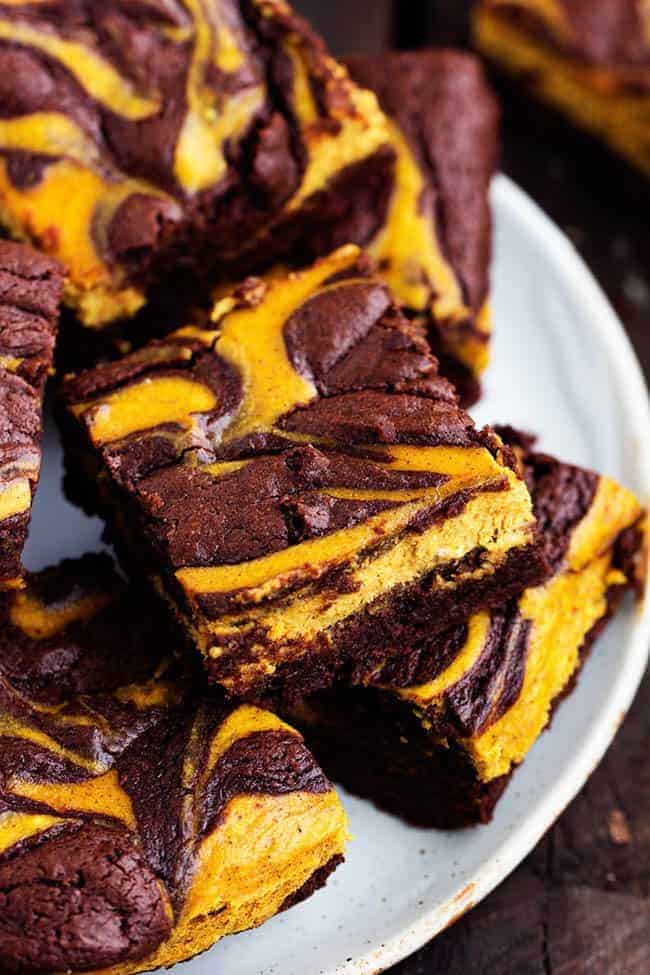 Perfectly moist and fudgy brownies swirled with pumpkin cheesecake. These are so rich and delicious and they make an amazing fall treat! pumpkin cheesecake brownies stacked on a white plate.