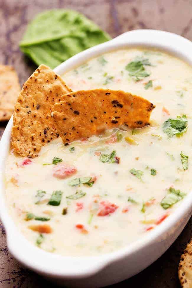 Melty white cheese, spinach, jalapeรฑos, and diced tomatoes come together in this incredible dip! This is a must make dip that you won't be able to get enough of! White Spinach Queso in a white serving dish with 2 tortilla chips.