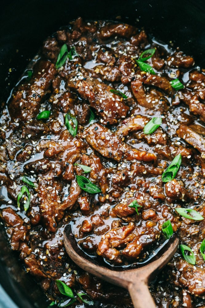 Amazing and flavorful beef that slow cooks to tender melt in your mouth perfection! This will be one of the best meals that you will make! Korean beef meat in the slow cooker being stirred with a wooden spoon.