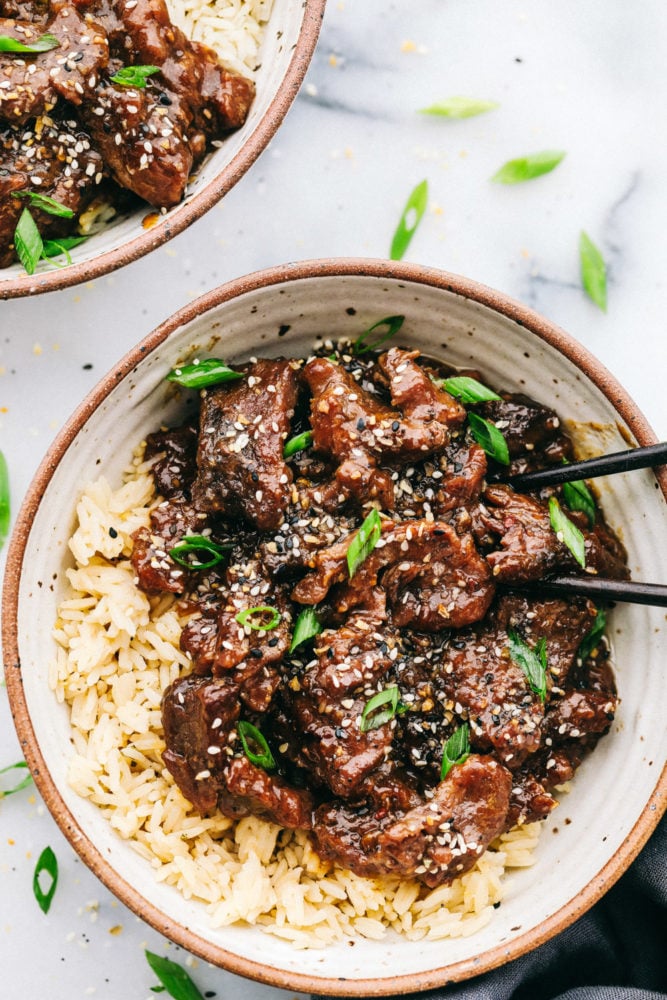 Amazing and flavorful beef that slow cooks to tender melt in your mouth perfection! This will be one of the best meals that you will make! Korean beef over rice in a bowl with two black chopsticks.