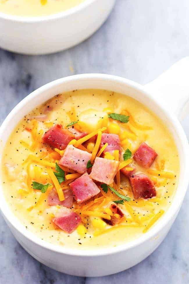 This hearty and delicious soup is full of ham, potatoes, and veggies. The real cheddar cheese inside adds such amazing flavor to this comforting soup! It became an instant favorite at our house! Ham and Potato Cheddar Soup in a white bowl.