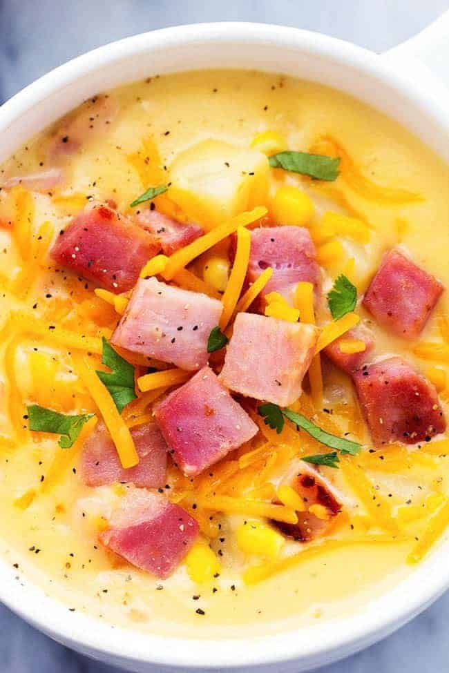 This hearty and delicious soup is full of ham, potatoes, and veggies. The real cheddar cheese inside adds such amazing flavor to this comforting soup! It became an instant favorite at our house! Ham and Potato Cheddar Soup in a white bowl.