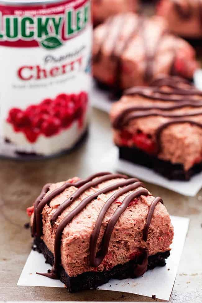 Delicious light and fluffy chocolate mouse with hidden cherries busting inside. This dessert is rich and creamy on top of an oreo crust and drizzled in chocolate. It will become an instant favorite with the first bite! Chocolate Cherry Mousse Bars with Lucky Leaf Cherry Filling in background