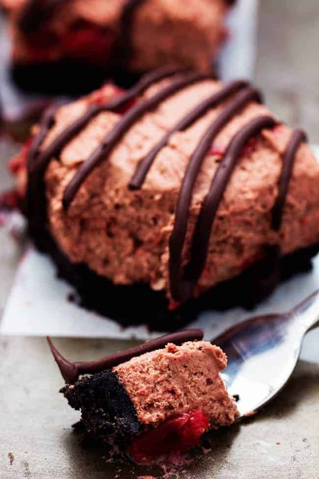 Delicious light and fluffy chocolate mouse with hidden cherries busting inside. This dessert is rich and creamy on top of an oreo crust and drizzled in chocolate. It will become an instant favorite with the first bite! Chocolate Cherry Mousse Bars with a small amount on fork