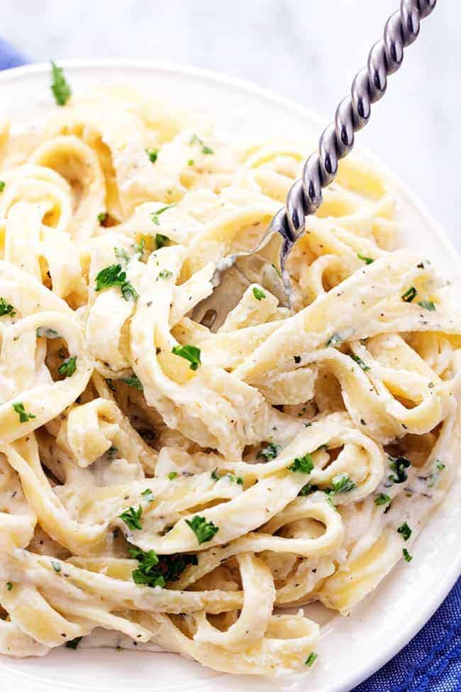 A lightened up garlic alfredo sauce that is delicious and creamy and coats the pasta perfectly! Half of the calories and you won't even be able to tell! Skinny Fettuccini Garlic Alfredo pasta in a bowl with a fork.