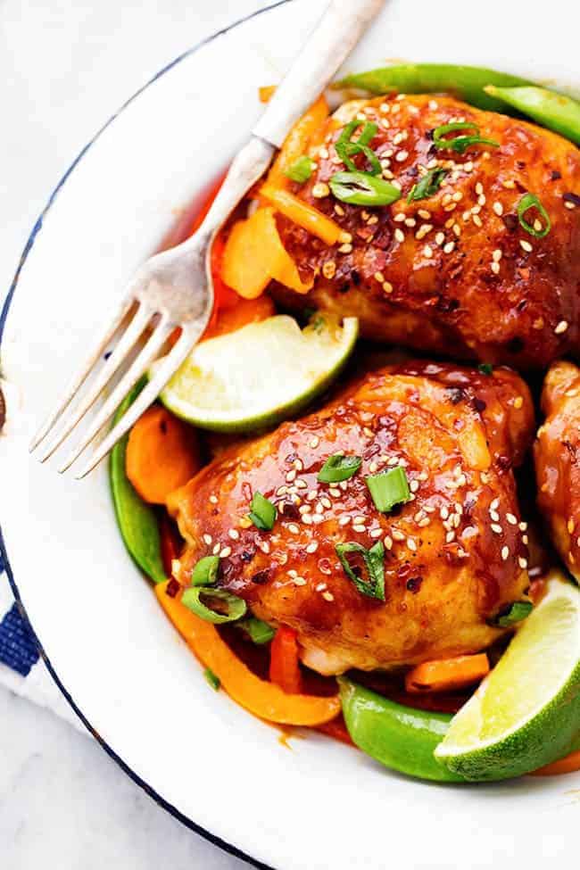 A 30 minute one skillet meal that is full of amazing flavor and veggies! The thai peanut sauce glazes the chicken perfectly and this will be a hit for dinner! Thai Peanut Skillet Chicken on a white plate with lime and other fresh vegetables.
