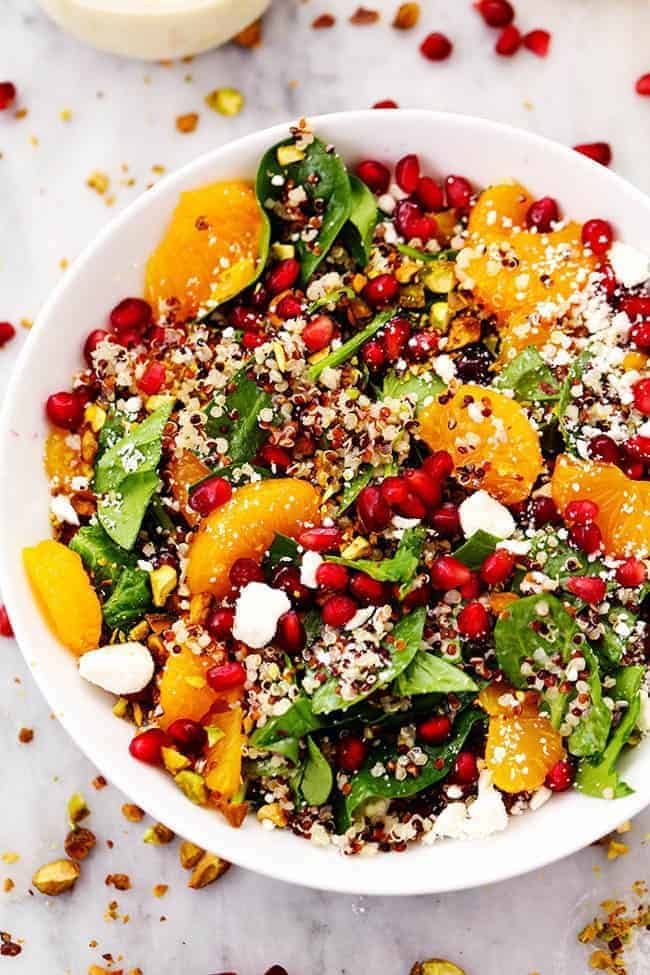 A mouthwatering winter salad with quinoa, spinach, mandarine oranges, and crunchy pistachios. Topped with a creamy lemon greek yogurt dressing and feta cheese this makes one unforgettable salad! WINTER POMEGRANATE ORANGE QUINOA SALAD WITH CREAMY LEMON GREEK YOGURT DRESSING IN A WHITE BOWL.