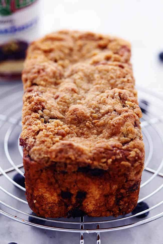 An amazingly moist muffin bread filled with blueberry pie filling. Topped with a crumb topping and drizzled in a lemon glaze this bread is incredible!ย Blueberry pie bread on a cooling rack fresh out of the oven.