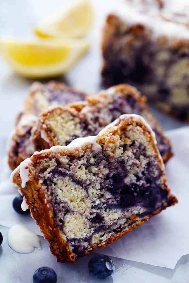 An amazingly moist muffin bread filled with blueberry pie filling. Topped with a crumb topping and drizzled in a lemon glaze this bread is incredible!ย Slices of blueberry pie bread with lemon glaze and fresh blueberries on the side.