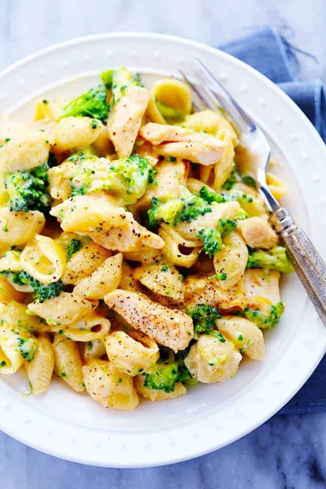 Ditch the boxed mac and cheese and make these amazingly creamy and cheesy chicken broccoli shells. This meal is sure to be a huge hit with the family! CHEESY CHICKEN BROCCOLI SHELLS ON A WHITE PLATE WITH A METAL FORK.